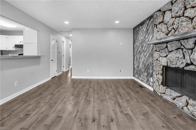 unfurnished living room featuring recessed lighting, baseboards, a stone fireplace, and wood finished floors