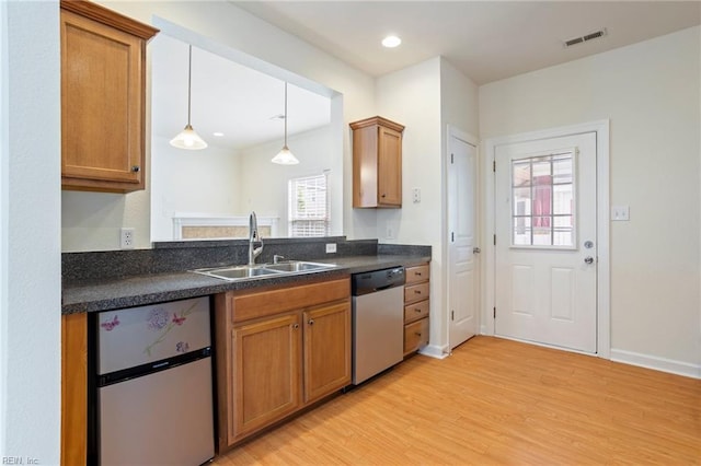kitchen featuring a sink, stainless steel appliances, light wood-type flooring, visible vents, and dark countertops