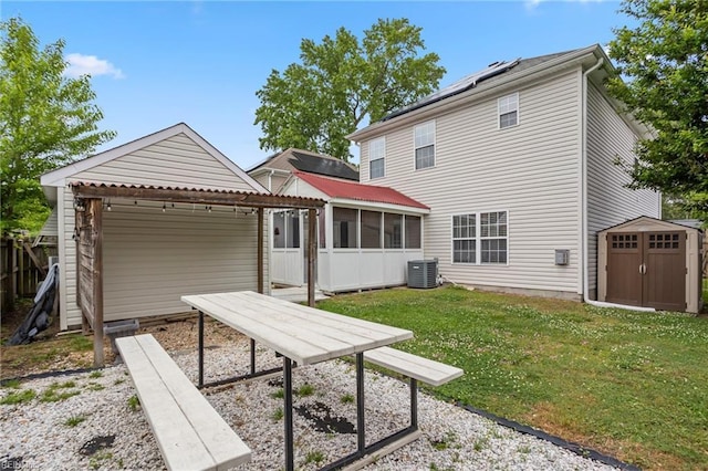 rear view of property with a storage unit, a sunroom, a yard, central AC unit, and an outbuilding