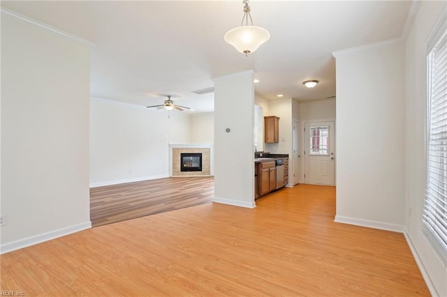 unfurnished living room with a ceiling fan, light wood-style flooring, baseboards, ornamental molding, and a glass covered fireplace