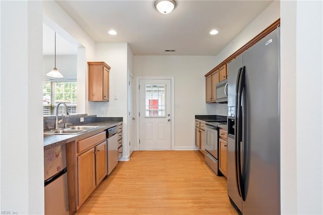 kitchen with a sink, brown cabinets, light wood-style flooring, dark countertops, and appliances with stainless steel finishes