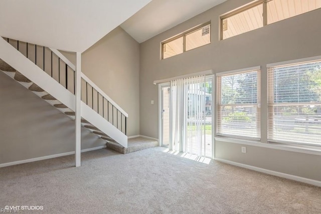carpeted entrance foyer featuring baseboards, a towering ceiling, and stairs