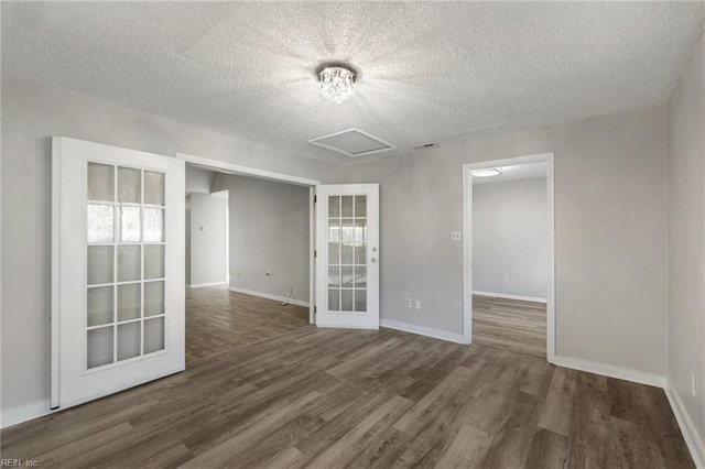 unfurnished room featuring a textured ceiling, wood finished floors, baseboards, and attic access