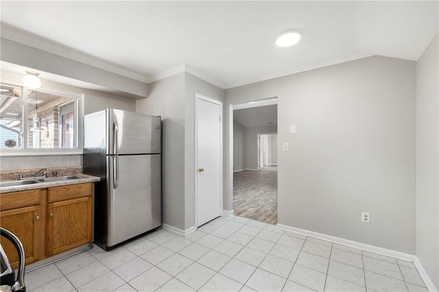 kitchen featuring freestanding refrigerator, brown cabinetry, a sink, baseboards, and crown molding