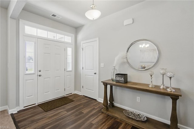 foyer entrance with an inviting chandelier, baseboards, dark wood-type flooring, and visible vents