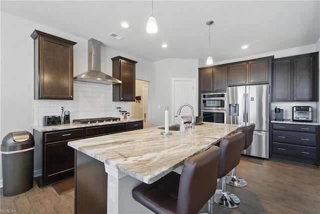 kitchen featuring visible vents, a sink, wall chimney exhaust hood, stainless steel appliances, and tasteful backsplash