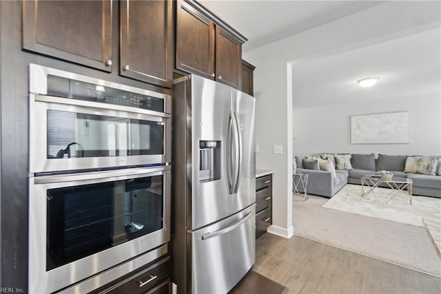 kitchen featuring baseboards, dark brown cabinetry, open floor plan, wood finished floors, and stainless steel appliances