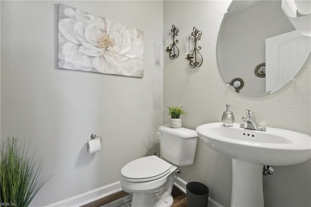 half bath with a sink, toilet, baseboards, and wood finished floors