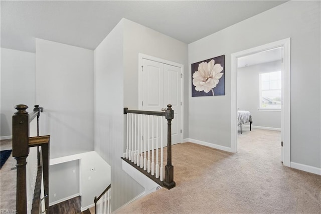 hallway featuring carpet, baseboards, and an upstairs landing