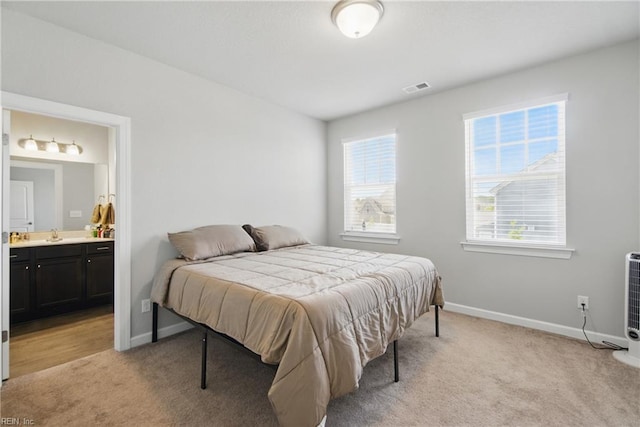 bedroom with ensuite bath, light colored carpet, baseboards, and visible vents