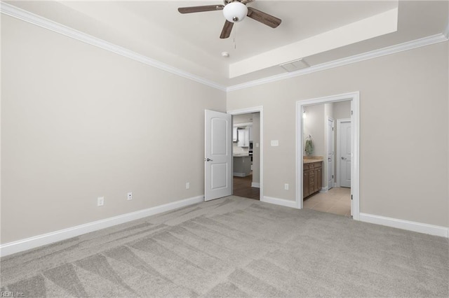 unfurnished bedroom with light carpet, a tray ceiling, crown molding, baseboards, and connected bathroom