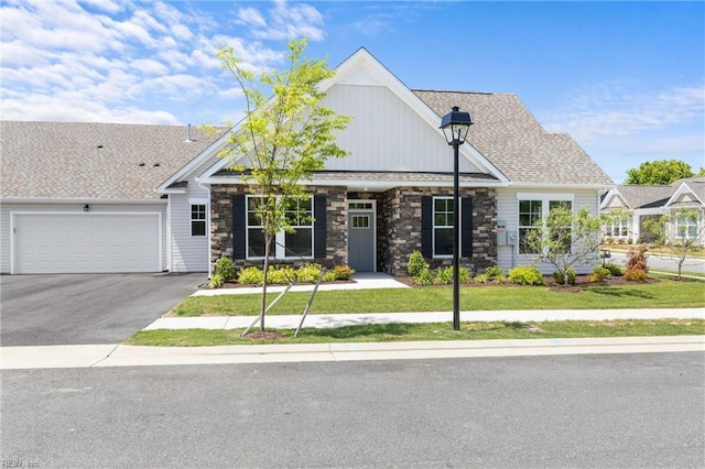 view of front facade featuring asphalt driveway, a garage, stone siding, a front yard, and board and batten siding