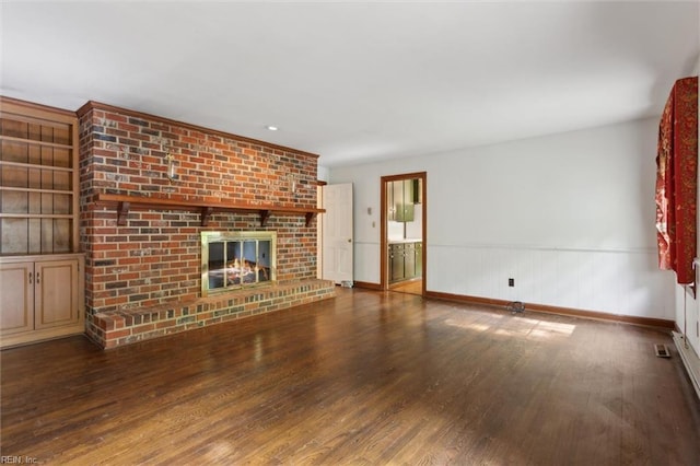 unfurnished living room featuring baseboards, a brick fireplace, wainscoting, and wood finished floors