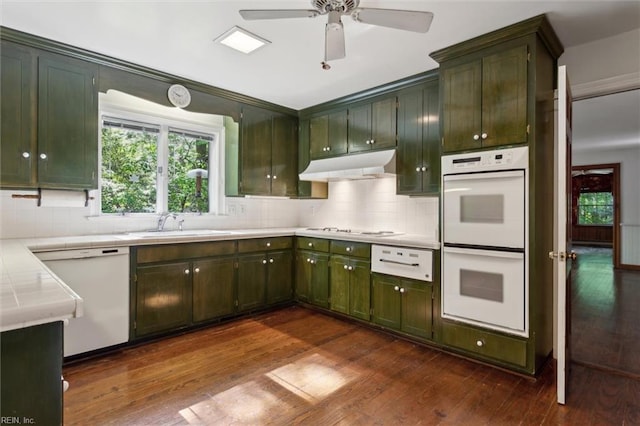 kitchen with under cabinet range hood, backsplash, dark wood finished floors, and white appliances