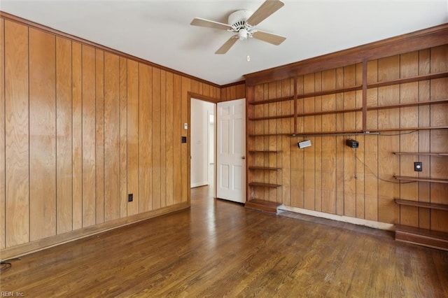 empty room featuring a ceiling fan, baseboards, wood walls, and wood finished floors