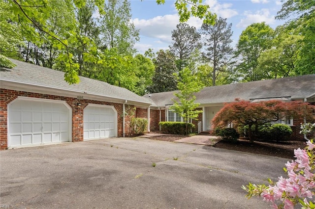 single story home with driveway, roof with shingles, brick siding, and an attached garage