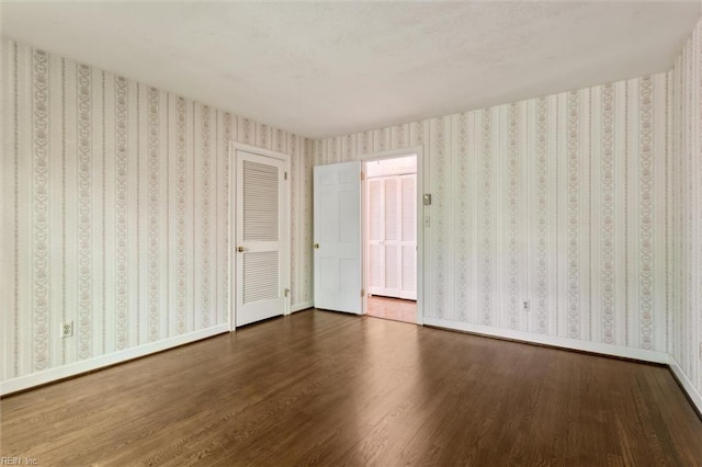 spare room with baseboards and dark wood-style floors
