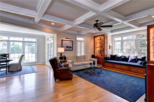 living room with light wood-type flooring, beamed ceiling, crown molding, coffered ceiling, and a ceiling fan