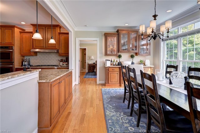 kitchen featuring multiple ovens, brown cabinets, a chandelier, under cabinet range hood, and light wood finished floors