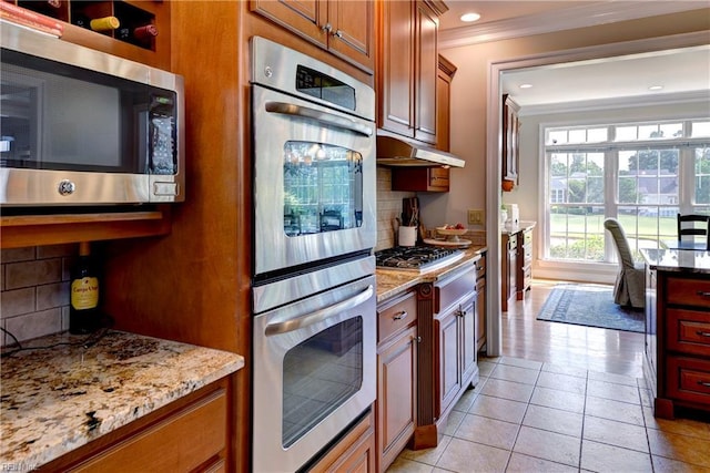 kitchen featuring appliances with stainless steel finishes, ornamental molding, under cabinet range hood, tasteful backsplash, and light stone countertops