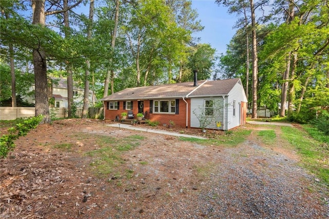 single story home featuring dirt driveway, brick siding, and fence