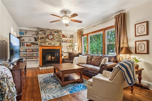 living room featuring built in shelves, a stone fireplace, a ceiling fan, and wood finished floors
