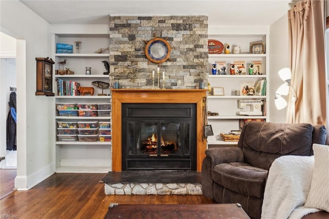 living room with built in features, wood finished floors, baseboards, and a stone fireplace