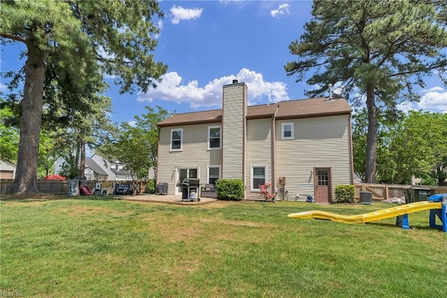 back of house featuring a fenced backyard, a deck, a chimney, and a lawn