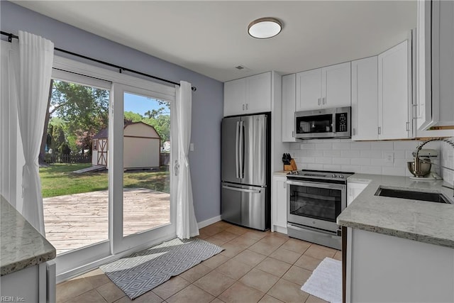 kitchen featuring a sink, stainless steel appliances, decorative backsplash, light tile patterned floors, and white cabinets