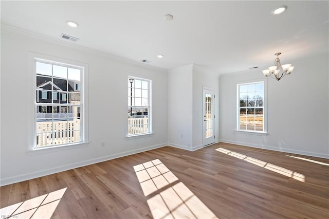 unfurnished room with an inviting chandelier, wood finished floors, crown molding, visible vents, and baseboards