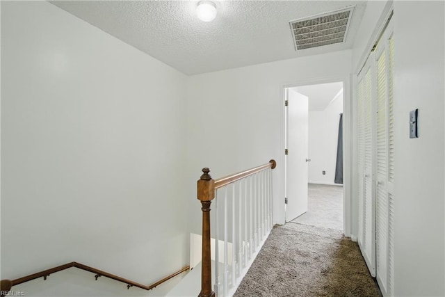 corridor featuring carpet, a textured ceiling, visible vents, and an upstairs landing