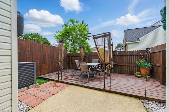 wooden terrace with a fenced backyard, outdoor dining area, and central AC unit