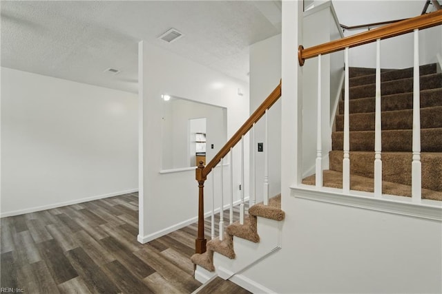 stairway featuring baseboards, visible vents, a textured ceiling, and wood finished floors