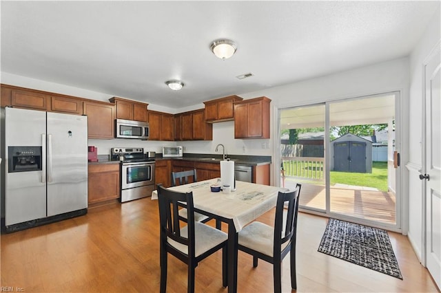 kitchen with light wood finished floors, a sink, dark countertops, stainless steel appliances, and visible vents