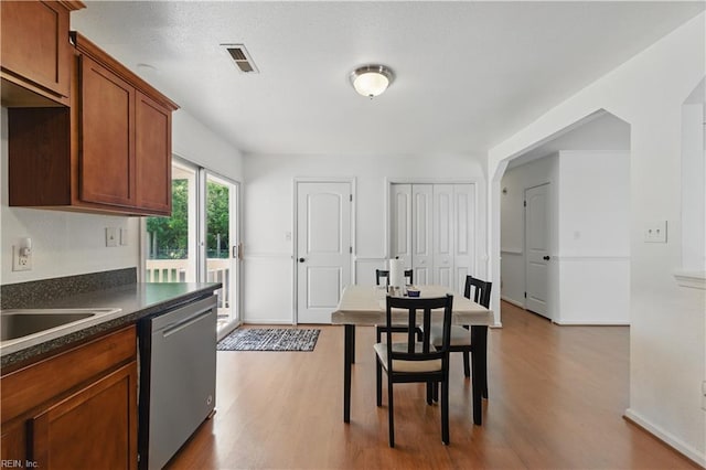 kitchen featuring wood finished floors, dark countertops, brown cabinetry, visible vents, and dishwasher