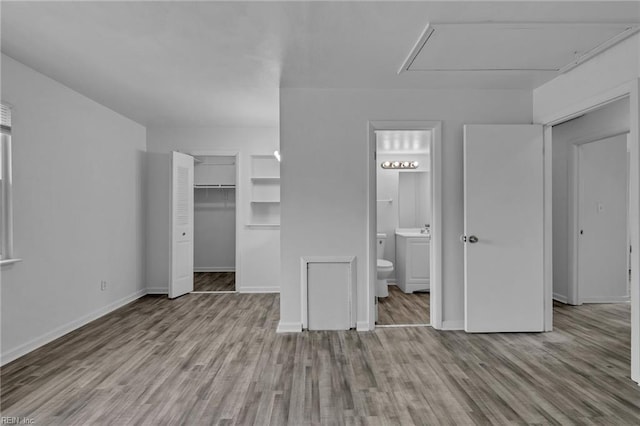 unfurnished bedroom with attic access, wood finished floors, baseboards, and ensuite bath