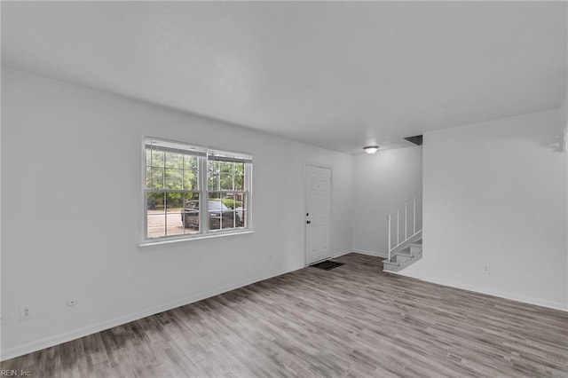 empty room featuring stairs, wood finished floors, and baseboards
