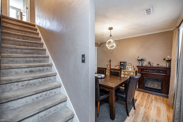 stairs with wood finished floors, a textured ceiling, visible vents, crown molding, and a glass covered fireplace