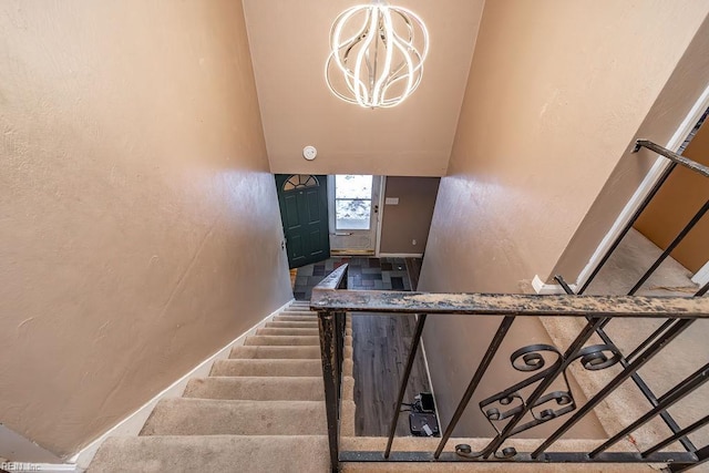 stairs with vaulted ceiling, a chandelier, a textured wall, and baseboards