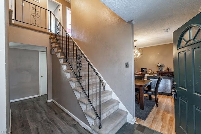 stairs featuring wood finished floors, a textured ceiling, visible vents, crown molding, and baseboards