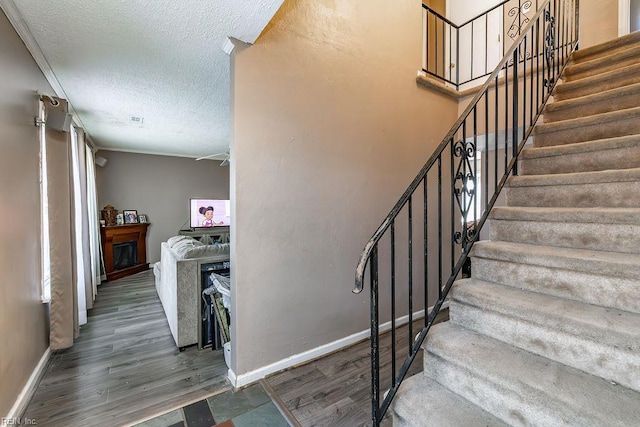 staircase with a textured ceiling, baseboards, and wood finished floors