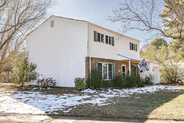 snow covered property featuring an attached garage and brick siding