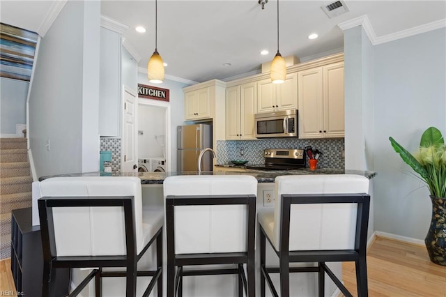 kitchen with a peninsula, stainless steel appliances, cream cabinetry, visible vents, and decorative backsplash