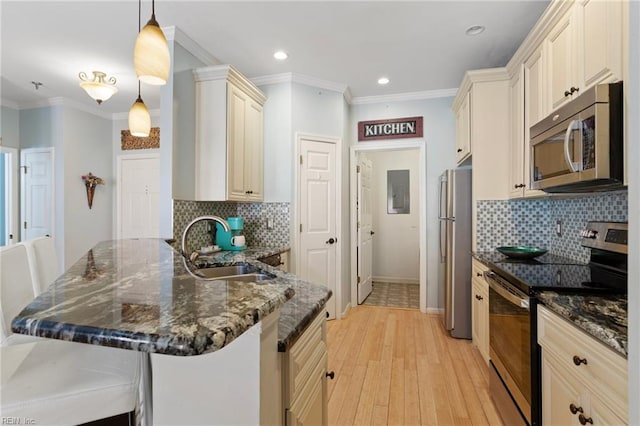 kitchen with light wood finished floors, a peninsula, a sink, stainless steel appliances, and ornamental molding