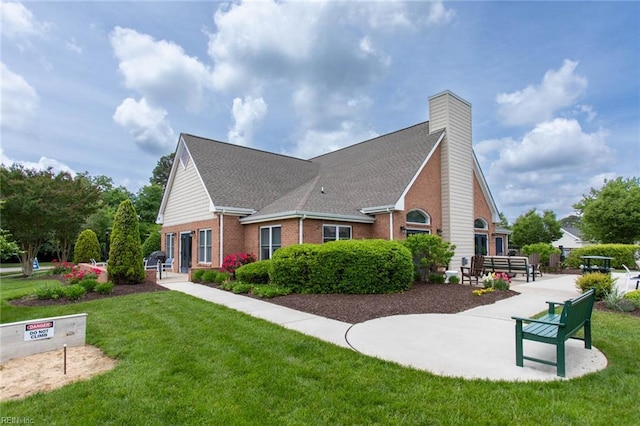 view of property exterior featuring a chimney, roof with shingles, brick siding, and a lawn