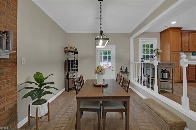 dining space with wood finished floors, baseboards, ornamental molding, and brick wall