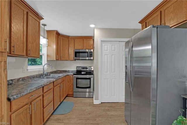 kitchen featuring appliances with stainless steel finishes, a sink, light wood-type flooring, brown cabinetry, and decorative light fixtures