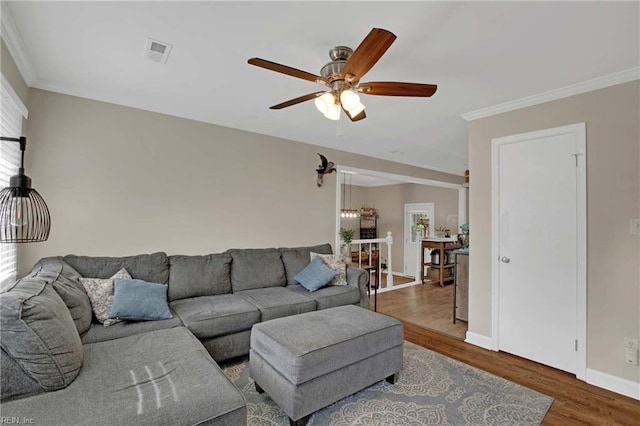 living area featuring wood finished floors, a ceiling fan, crown molding, and baseboards
