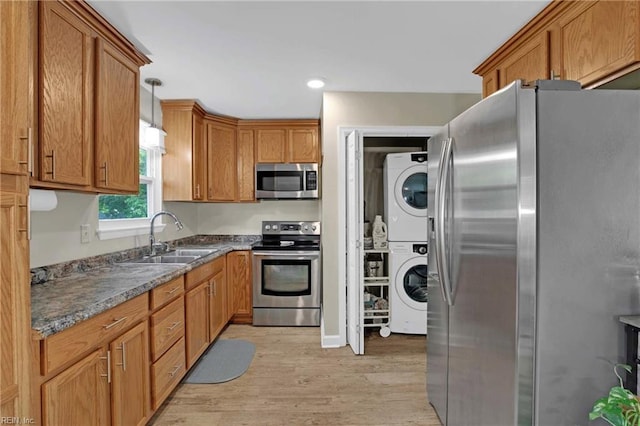 kitchen featuring appliances with stainless steel finishes, stacked washer / drying machine, a sink, light wood-style floors, and brown cabinets