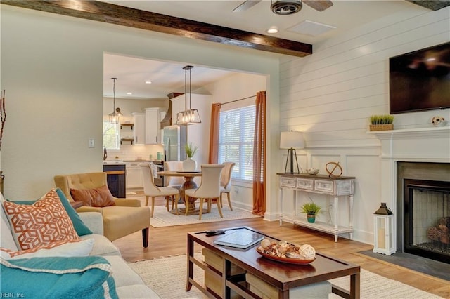 living room with beam ceiling, light wood-type flooring, recessed lighting, ceiling fan, and a fireplace with flush hearth